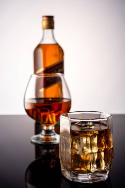 Karanlık bir arka planda buzlu viski. Arka planda bir bardak viski ve bir şişe viski.