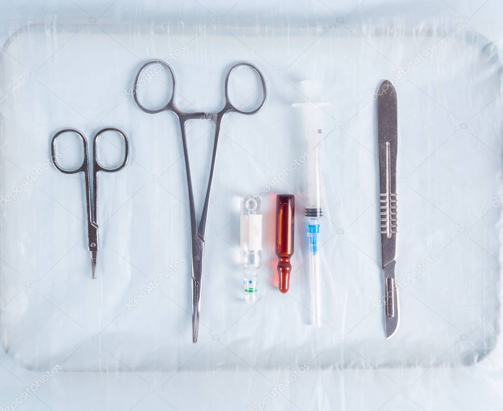 Scalpels, medical clamps, syringe in a metal tray