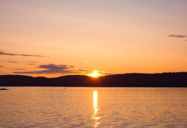 Gölde gün batımı. Güneş karanlık bir orman şeridinin arkasında saklanıyor. Turuncu gökyüzünde sirk bulutları