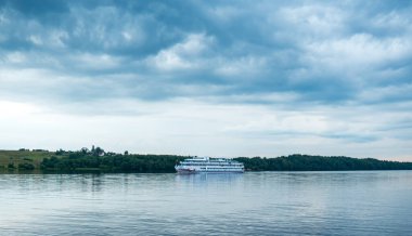 Bulutlu havada nehrin manzarası. Yolcu gemisi nehir boyunca ilerliyor.