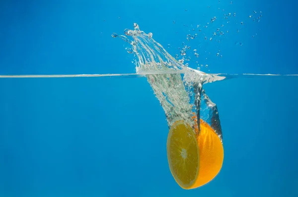 Éclaboussures d'orange dans l'eau avec fond bleu Images De Stock Libres De Droits