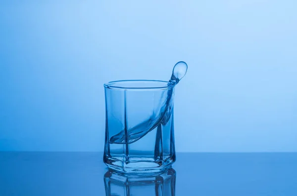 Выплеск в стакане воды на голубом фоне — стоковое фото
