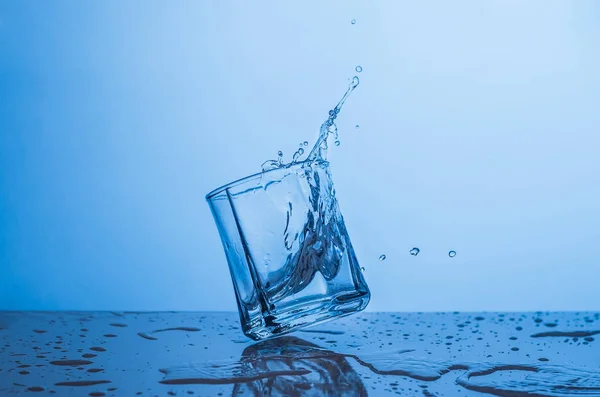 Splash em um copo de água em um fundo azul — Fotografia de Stock
