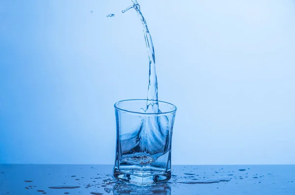 Выплеск в стакане воды на голубом фоне — стоковое фото