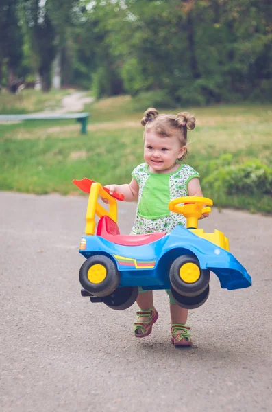 The little girl drags the kids car on the road — Stock Photo, Image