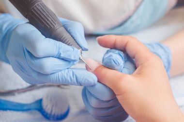 Lastik eldiven manikür ustası bir manikür, tırnak cilası makine yardımıyla bir kadın üzerinde çivi yapar.