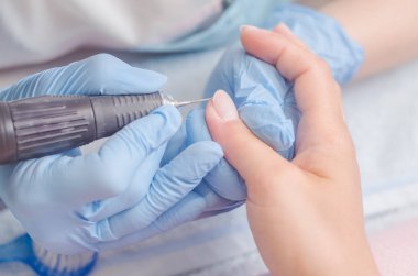 Lastik eldiven manikür ustası bir manikür, tırnak cilası makine yardımıyla bir kadın üzerinde çivi yapar.