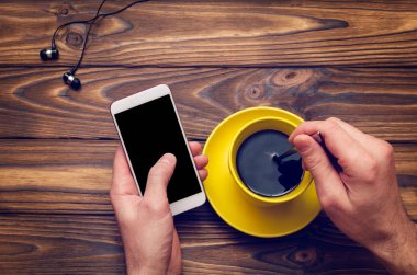 Bir cep telefonu ile bir boş siyah perde ve eski ahşap masa bir kafede sarı bir fincan kahve mockup görüntü