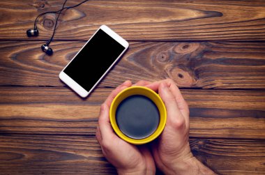 Bir cep telefonu ile bir boş siyah perde ve eski ahşap masa bir kafede sarı bir fincan kahve mockup görüntü