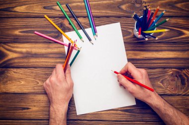 Renkli kalemler ve boş bir sayfa ile ahşap bir masa üzerinde eller