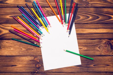 Boş kağıt ve ahşap bir masa üzerinde renkli kalemler