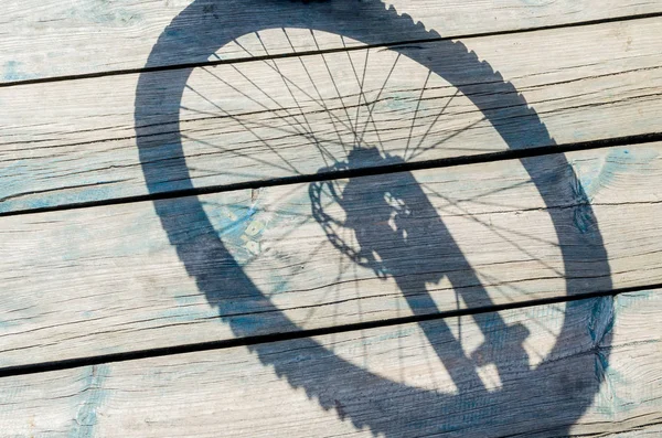 Schatten von einem Fahrradrad auf einem hölzernen Hintergrund — Stockfoto