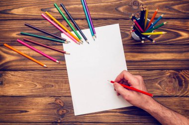Renkli kalemler ve boş bir sayfa ile ahşap bir masa üzerinde eller