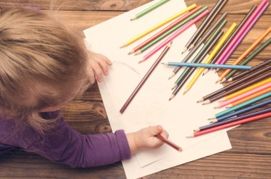 Küçük kız tahta masaya kalemle çiziyor.