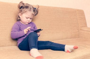 Küçük kız koltukta oturan smartphone oyun