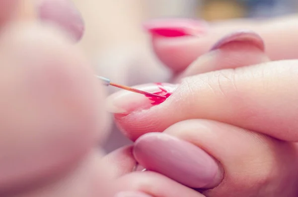 Manicurist paints nails with red lacquer in the salon
