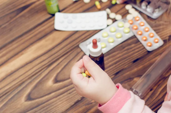 Children's hands with medicines on a wooden table. A small child left unattended plays dangerous drugs