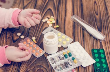 Ahşap bir masa üzerinde ilaçlarla çocuk eller. Küçük bir çocuk katılımsız çalış tehlikeli uyuşturucu yaptı.