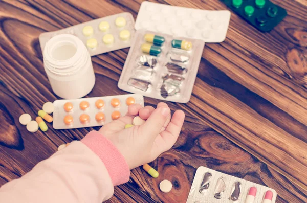 Children's hands with medicines on a wooden table. A small child left unattended plays dangerous drugs