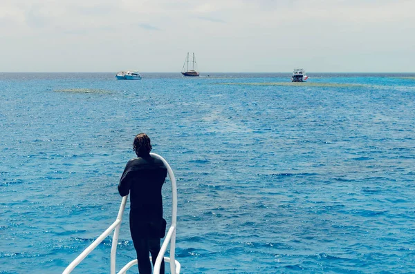 Um homem de fato de mergulho está no convés de um navio e olha para a distância — Fotografia de Stock