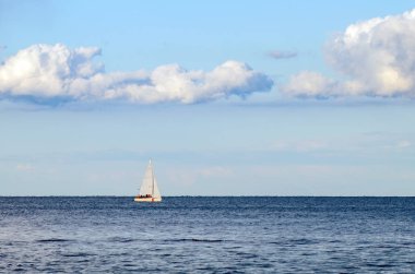 Denizin arka planında beyaz yelkenli bir yat ve bulutlarda gökyüzü