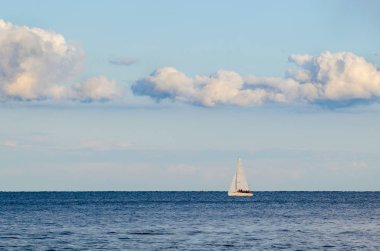 Denizin arka planında beyaz yelkenli bir yat ve bulutlarda gökyüzü