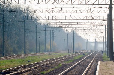 Demiryolu rayları ve destek direkleriyle sisli bir bahar sabahı tren istasyonunda