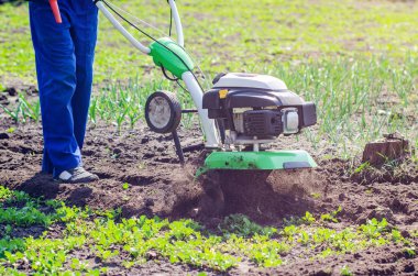 Bir adam bir bahar bahçesinde ekiciyle toprağı sürüyor.