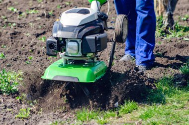 Bir adam bir bahar bahçesinde ekiciyle toprağı sürüyor.