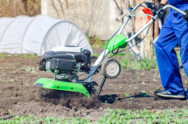 Um homem arado a terra com um cultivador em um jardim de primavera — Fotografia de Stock