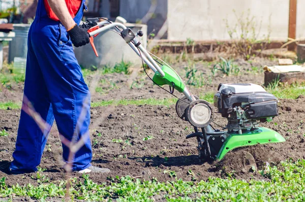 Un uomo aratura la terra con un coltivatore in un giardino primaverile — Foto Stock