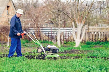 Bir adam bir bahar bahçesinde ekiciyle toprağı sürüyor.
