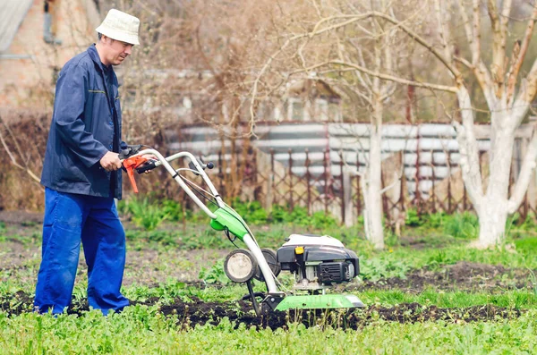 Een man ploegt het land met een cultivator in een lentetuin — Stockfoto