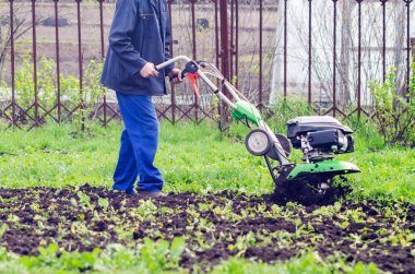 Bir adam baharda ekiciyle toprağı işliyor.