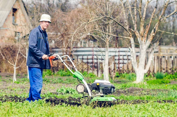 Um homem cultiva a terra com um cultivador em um jardim de primavera — Fotografia de Stock