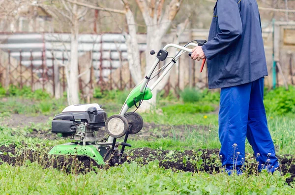 Un uomo coltiva la terra con un coltivatore in un giardino primaverile — Foto Stock