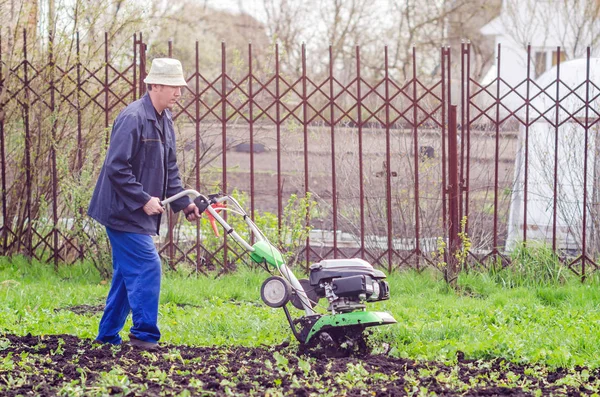 Een man cultiveert het land met een cultivator in een lentetuin — Stockfoto