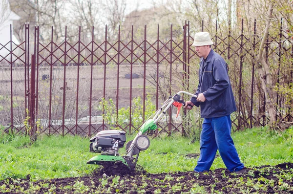 Ένας άνθρωπος οργώνει τη γη με έναν καλλιεργητή σε έναν κήπο άνοιξη — Φωτογραφία Αρχείου