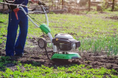 Bir adam bir bahar bahçesinde ekiciyle toprağı sürüyor.