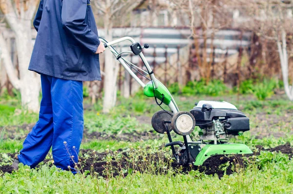 Un uomo aratura la terra con un coltivatore in un giardino primaverile — Foto Stock