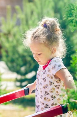 Küçük bir kızın portresi güneş ışığında bir spor sahasında yatay bir çubukta egzersiz yapıyor..