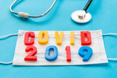 Stetoskop ve tıbbi solunum maskesi, mavi arkaplandaki virüslere karşı korunmak için 2019 yazıtlı..