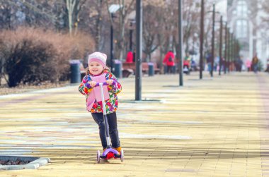 Şehir sokağında scooter süren küçük bir kız.