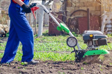 Bir adam bir bahar bahçesinde ekiciyle toprağı sürüyor..
