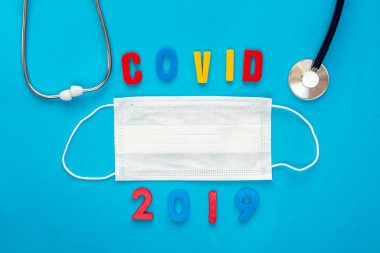 Stetoskop ve tıbbi solunum maskesi, mavi arkaplandaki virüslere karşı korunmak için 2019 yazıtlı..
