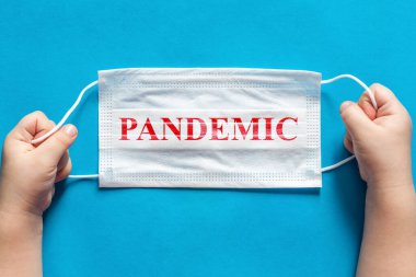 Çocukların ellerinde mavi arka planda virüslere karşı korunmak için kullanılan tıbbi solunum maskesi var..