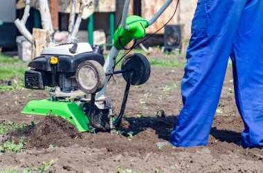Bir adam bir bahar bahçesinde ekiciyle toprağı sürüyor..