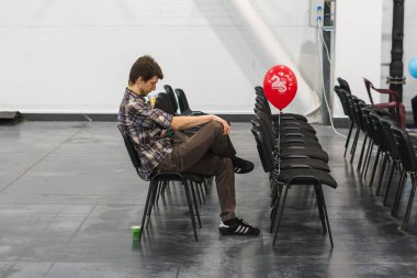 Kyiv, Ukrayna, 28 Şubat 2020: Genç bir adam sandalyede tek başına oturuyor ve akıllı telefondan bir şeye bakıyor.