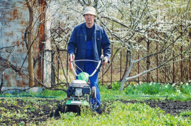 Bir adam baharda ekiciyle toprağı işliyor..