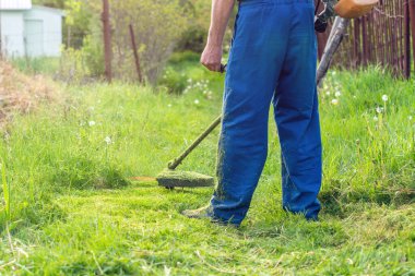 Bahçıvan bahar bahçesinde bir budama makinesiyle çimleri biçer.